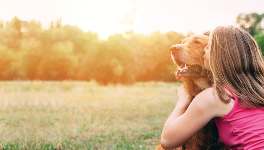 Donna seduta fuori in un campo con il suo cane mentre gli bacia il muso