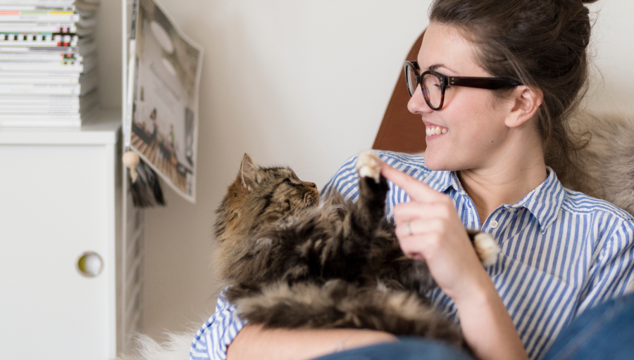 Una donna seduta con il suo gatto in braccio mentre gli tocca la zampa con un dito
