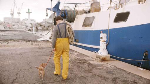 pescatore che porta a spasso il cane accanto a un peschereccio